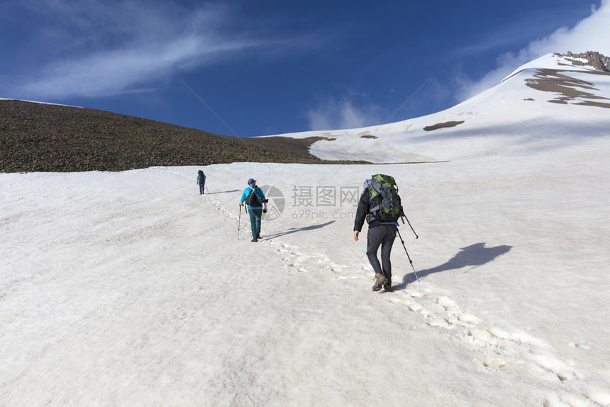 一群背着包的旅游者在雪山上徒步旅行游客从山坡上爬到雪顶峰太阳自由冒险图片