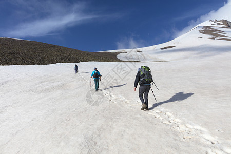 一群背着包的旅游者在雪山上徒步旅行游客从山坡上爬到雪顶峰太阳自由冒险图片