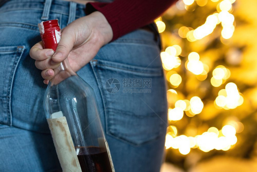 白色的圣诞树前人拿着一瓶酒圣诞节和新年喝得太多女人圣诞树前的拿着一瓶酒气泡辉光图片