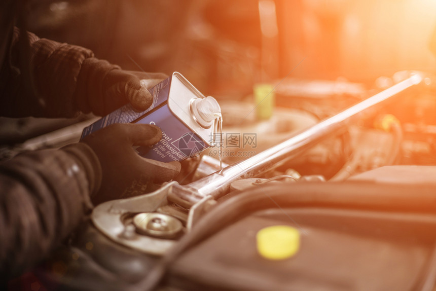 工人检查机械制动DOT4冷却器流体在一辆汽车里从时装的金属瓶子和日落颜色变化图片