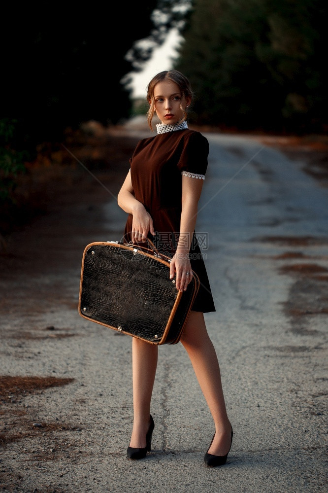 成人独自的秋天一个年轻漂亮的女孩穿着棕色裙子旧式的站台手里拿着黑色提箱在一条废弃的路上图片
