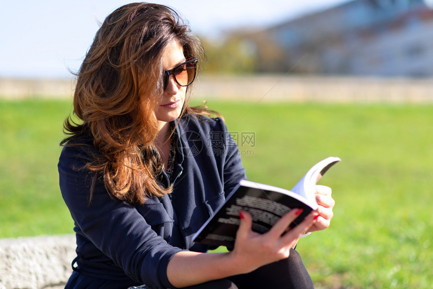 美丽的年轻女穿着漂亮的发型和太阳镜坐在户外看书阳光明媚的一天可爱文学知识图片