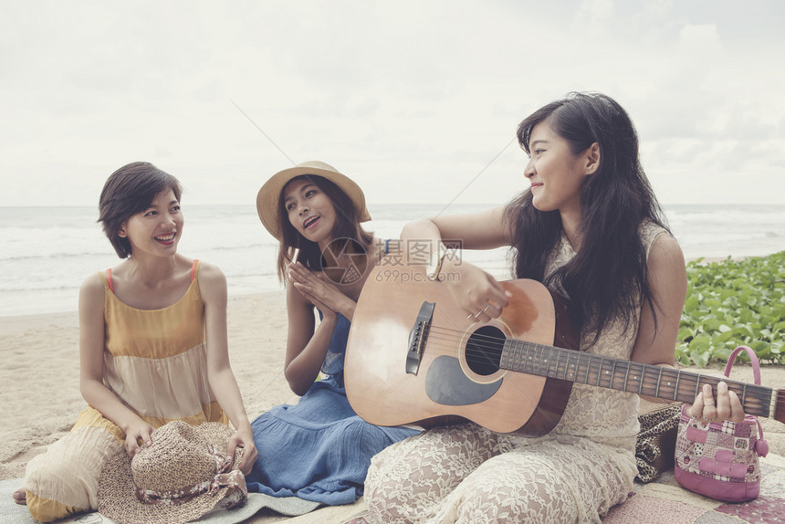 一种年青的亚洲女朋友度假在海边弹吉他和唱一首歌玩友谊图片