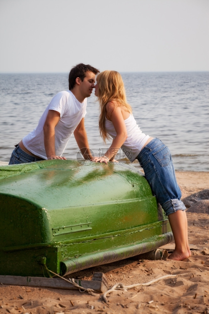 金沙在旧船附近的海滩上亲吻一对漂亮的夫妇蓝色水图片