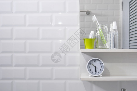 牙膏架子时间酒精早晨玻璃瓶中的牙刷小绿色桶中的牙膏在现代浴室的白色瓷砖墙上贴着时钟和镜子的洗手液喷雾以及个人配件背景