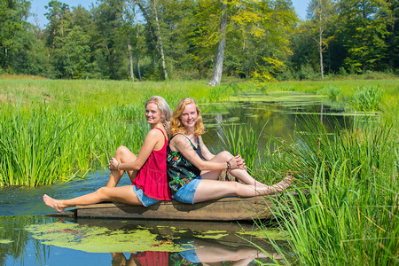 乐趣两名年轻的天主教女青年坐在自然界的溪流上植物喜悦图片