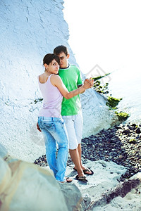 年轻情侣在阳光明媚的早晨在岩石海岸度过浪漫时光亲热海洋多岩石的图片