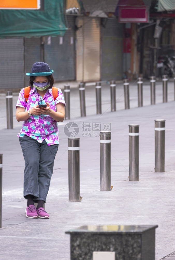 社区障碍女士使用智能手机的亚洲女旅游客在垂直架子上街行走时站在一排金属屏障之间同时使用智能手机图片