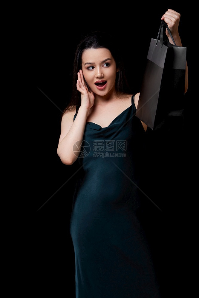 客户享受时髦的身着深绿裙子的年轻美女手里拿着黑纸购物袋在色孤立的背景下被困在她手上图片