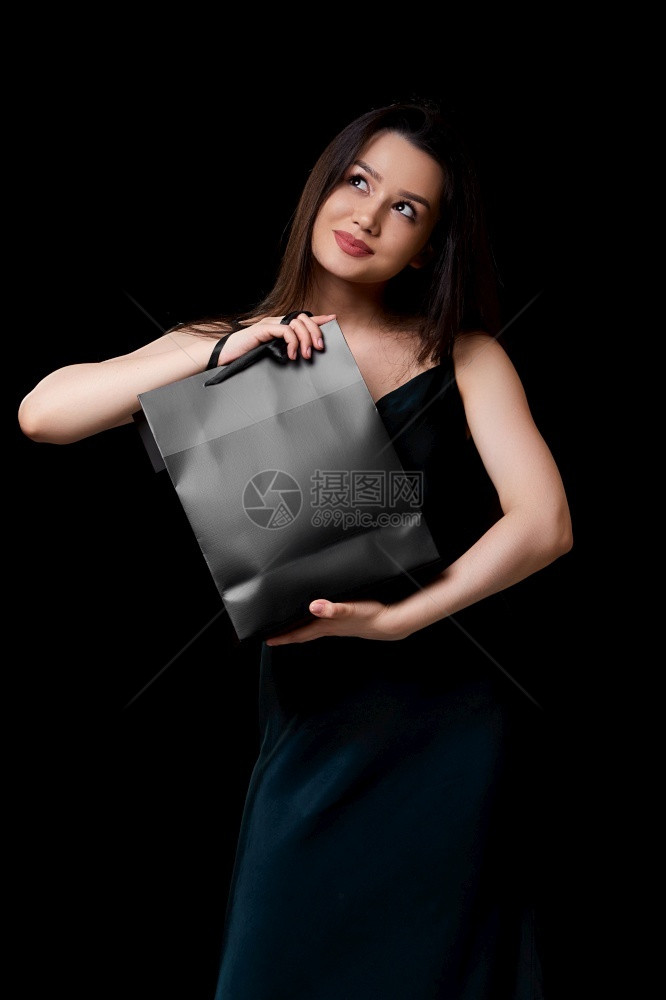 黑暗的店铺礼物身着深绿裙子的年轻美女手里拿着黑纸购物袋在色孤立的背景下被困在她手上图片