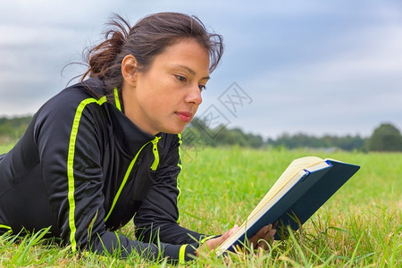严肃的躺在草丛读书中的欧裔妇女头发自然图片