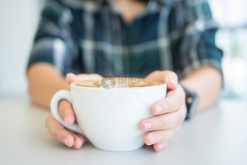 温暖的女人手拿着白咖啡杯是木桌上的一张拿铁咖啡桌复古风格从顶部看到奶泡的沫白色香气图片