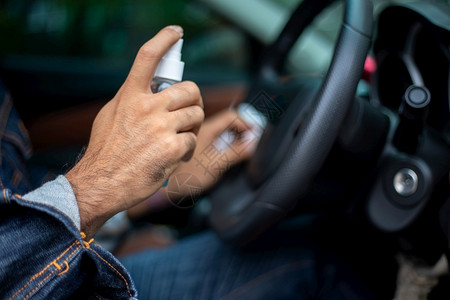 亚洲男子使用喷洒酒精清洁汽车以保护冠状的亚洲男子干净为了药物图片