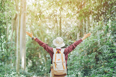 潮流当道自由旅游行者年轻女孩带着背包举起手在森林中享受美丽的大自然背景
