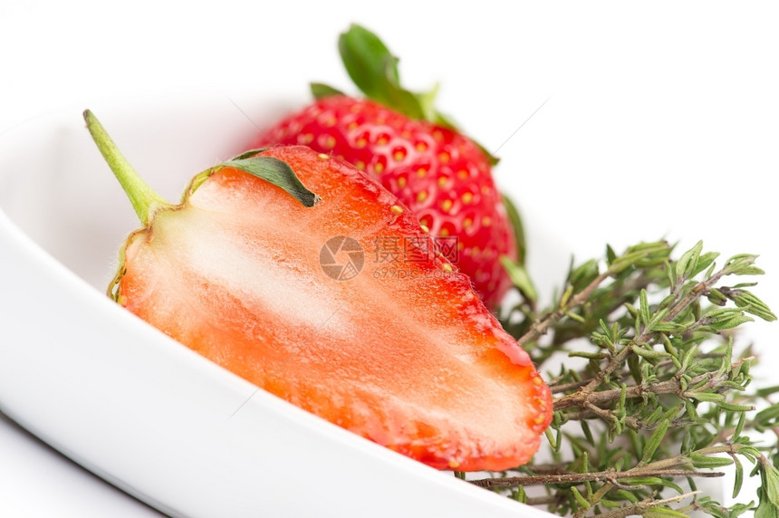 水果将新鲜多汁的成熟红草莓减半显示白碗中的肉或纸浆结构并配有一串新鲜迷迭香剂用作味调和烹饪成分维生素用过的图片