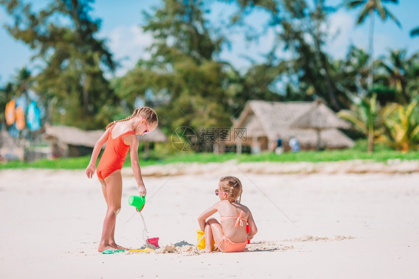 岛享受欢笑的小女孩在热带海滩玩得很开心一起玩做沙城堡暑假时在海滩上的小女孩儿们在夏天度假的时候俏皮图片
