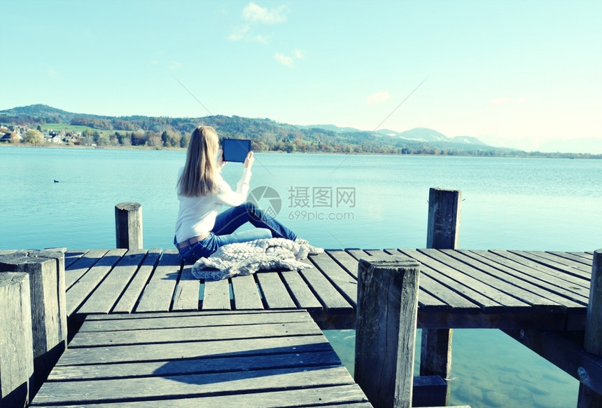 便携的柴金支撑女孩在木制码头的石板上对着瑞士湖阅读图片