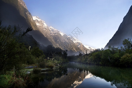 山中第一道光线反映新西兰密尔福德轨道的河谷溪流结石自然远景图片
