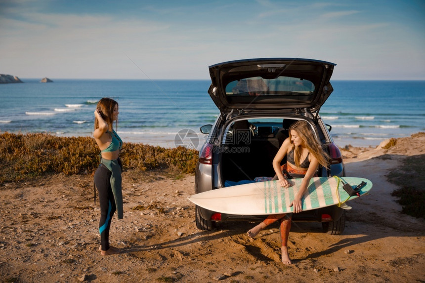 海滩两个美丽的冲浪女郎与她的车在海岸线附近并准备冲浪坐着的比基尼图片