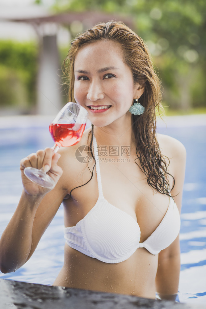 女士玻璃脸泳池中比基尼女人和一杯红饮料图片