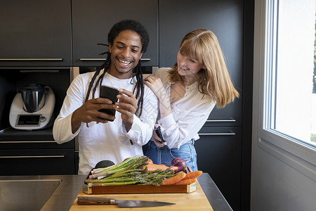 在厨房里用手机和蔬菜板健康生活概念使用移动电话的不同种族群体中的年轻一对青夫妇健康生活的概念女士药片年轻的背景图片
