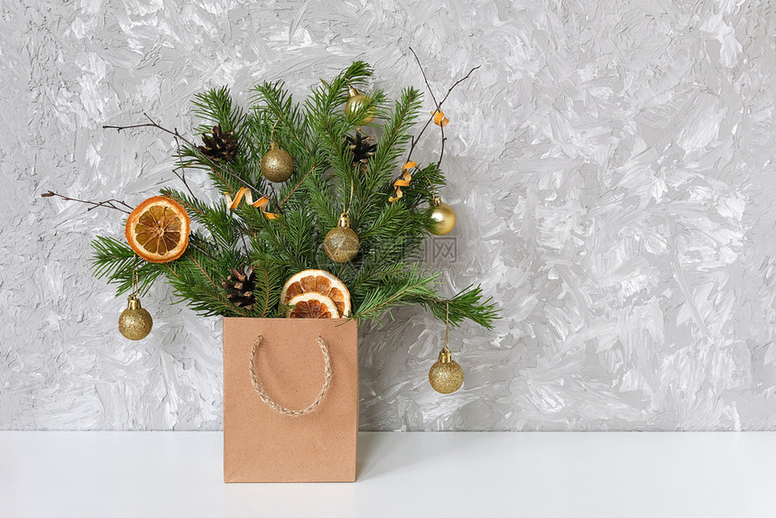 包裹云杉树枝的冬季节日花束装饰着金色的球桌上工艺包中锥体靠在灰色混凝土墙上圣诞节或新年概念复制空间模板用于明信片文字设计的云杉树图片