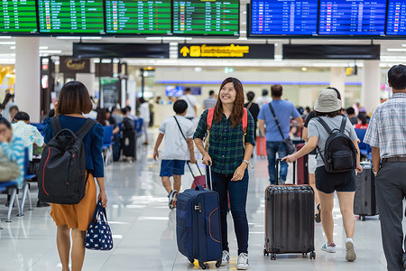 商务办公登入延迟朋友们手提箱携带行李的亚洲旅者在现代机场飞行信息屏幕登入旅行和带有技术概念的交通检查时看飞行机板上的载有李亚洲旅者背景