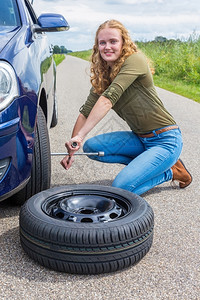 解放外部延迟年轻的欧洲女青在乡村公路上换车轮胎图片