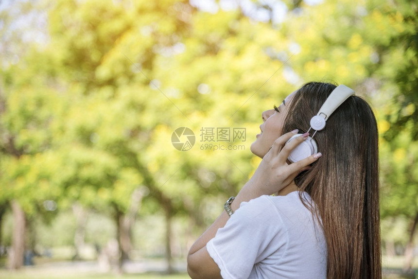 技术小工具电话快乐听音的少女在公园户外智能听音乐时耳机戴为健康妇女提供音乐心理治疗师爱幸福的女图片