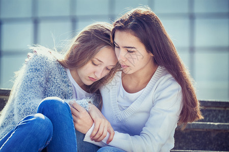 明亮的中学女青少年因为问题而哭泣她的朋友对坐在楼梯上她身的充满同情和秋天背景图片