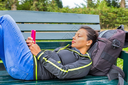 交流躺在长凳上操作移动电话的欧洲妇女休息应用程序图片