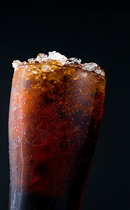 可乐冰在暗底背景与复制空间隔绝的玻璃杯中用冰隔离的软饮料在透明玻璃表面有一滴水那里腐烂的苏打设计图片