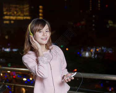 亚洲人肖像身戴黄色耳机手持背景为城市灯光的马来西亚女她戴着黄耳机称呼图片