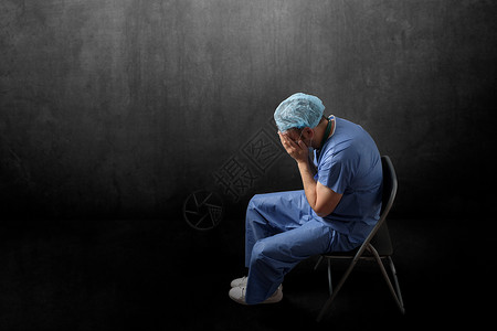 舍纳塔根坐在一间黑暗房的位悲伤疲劳的医生侧面景象坐在一间黑暗房里的一位疲惫医生专业白种人背景图片
