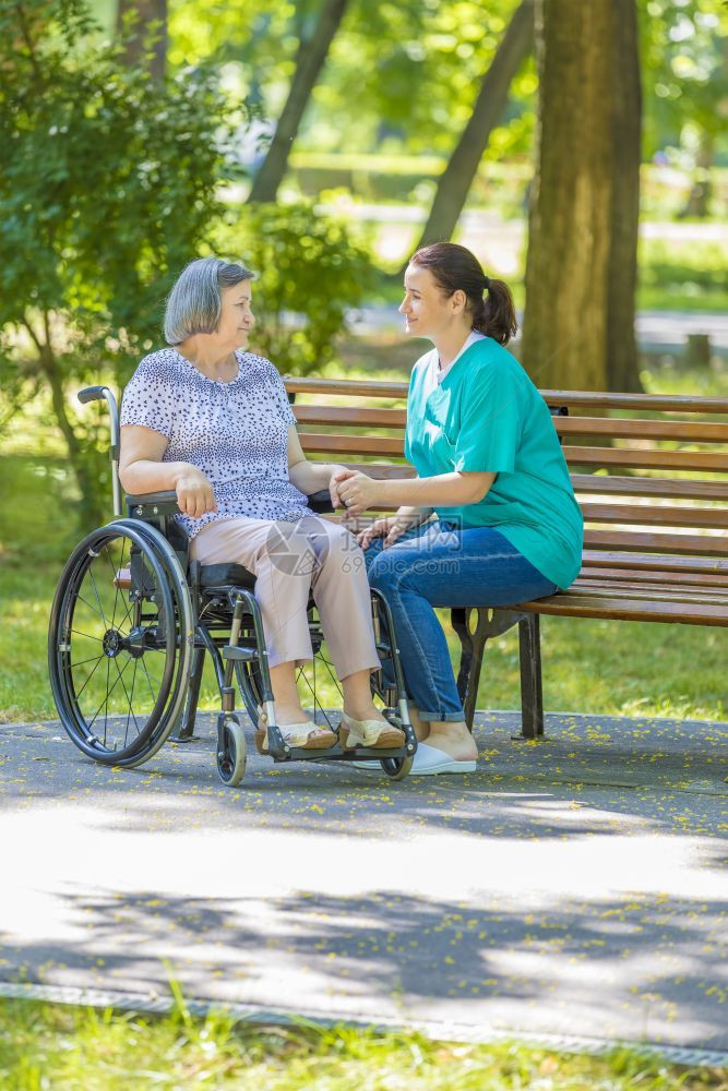 淑女残疾人在夏季公园户外轮椅运动室与残疾老年妇女交谈的护理员截瘫图片