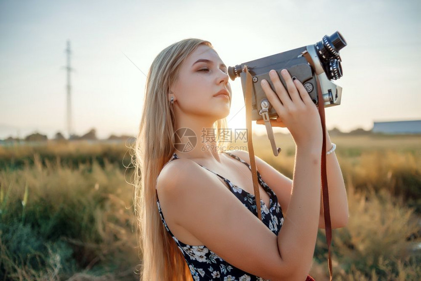漂亮的日落时在葡萄田中用古老的录像机拍摄着花粉印刷服装的金发女孩肖像快乐的保持图片