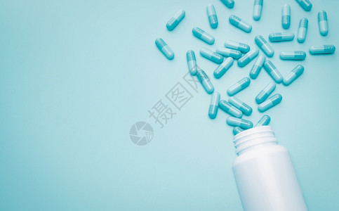 表面上的药丸包装在线的治疗蓝胶囊药丸从白塑料瓶中散布出来在蓝底本的白塑料药瓶上散发抗生素药物或超级诱虫概念健康预算和政策抗生素药物过度使用插画