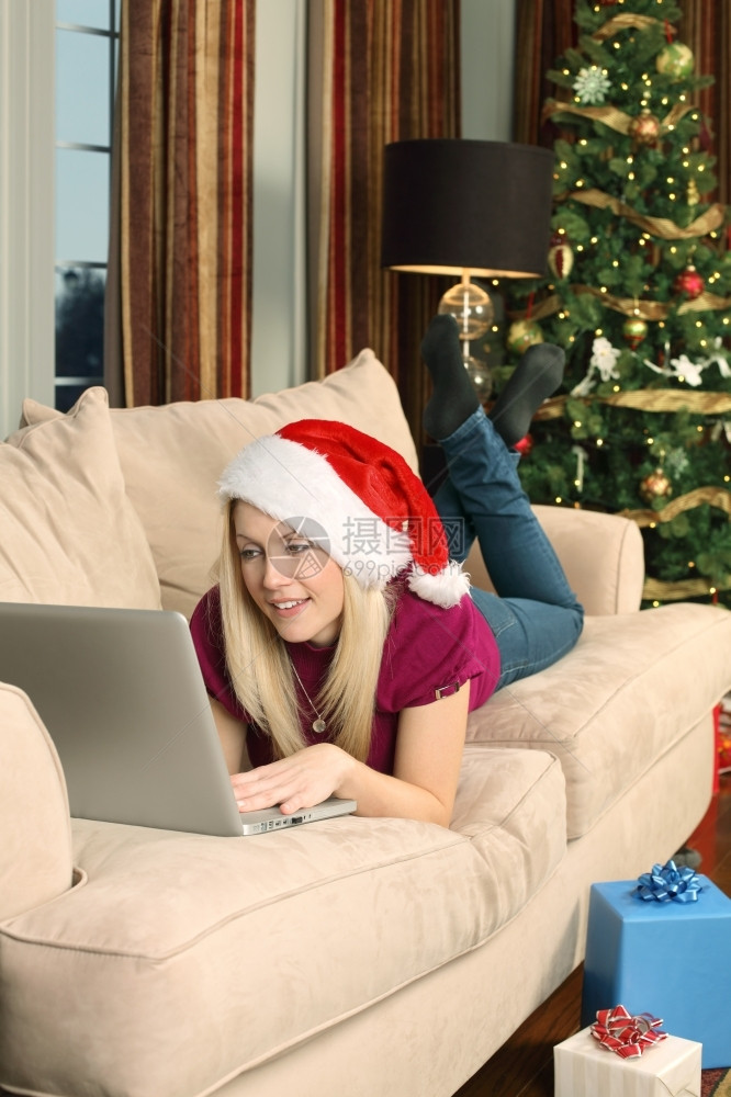 一位美丽的金发女坐在沙上用笔记本电脑买圣诞礼物的照片在线铺设相机图片