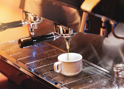 现代的浓缩咖啡机冲泡倒入店的玻璃杯中浓缩咖啡从机中倒出滴进入图片