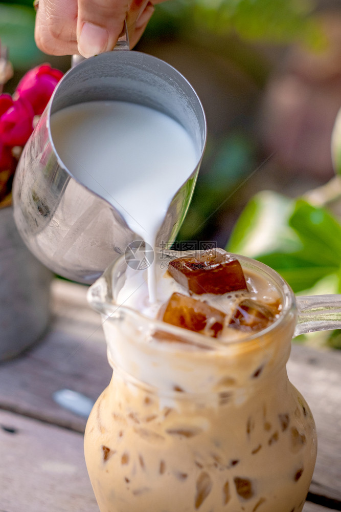 餐厅将牛奶倒在玻璃杯中加拿铁咖啡和木制桌底冰有条纹的寒冷图片