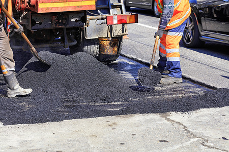 黑色的道路工人作组以新鲜热沥青更路段用的热沥青加铲子并在地面上均匀分配工组人员在修筑的公路现场平均分发热沥青和手动用铲子处理的在背景图片