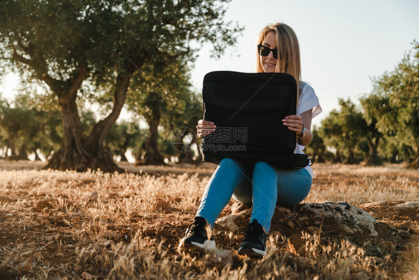 坐着的在橄榄树田里的拥有笔记本电脑的年轻妇女分析师报告图片