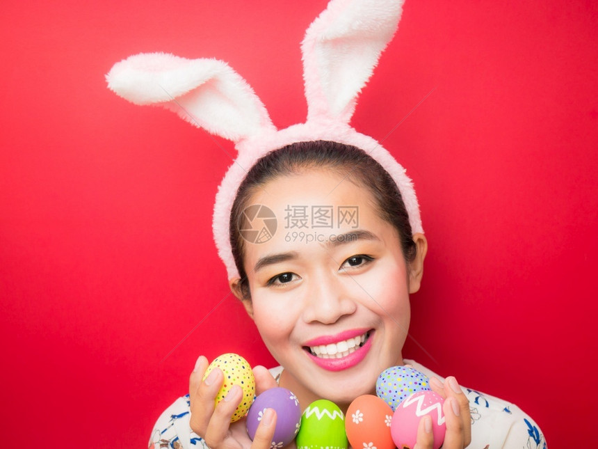 一种复活节时戴兔子耳朵头带和携复活节鸡蛋的妇女有吸引力的年轻女微笑在明亮的红色背景上笑好的手图片