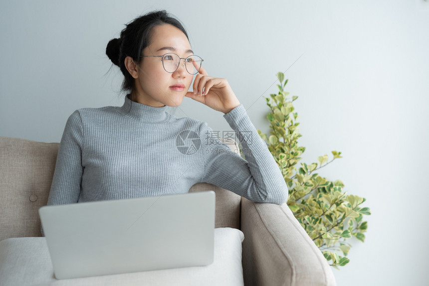 亚洲人公司的在家中用笔记本电脑工作的年轻亚洲妇女坐在桌子上手靠着下巴躺员工图片