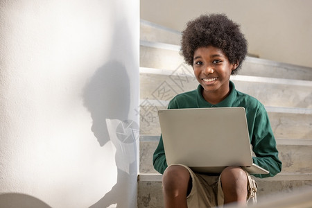 一名非洲卷发男孩坐在楼下走廊一栋的台笔记本电脑上新冠在下面电信图片