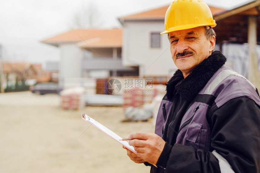 建造Caucasian高级男子建筑工一般人建筑承包商的肖像他们身着黄色保护头盔手持钢笔和现场数据报告项目文件核对检查专业知识保护图片