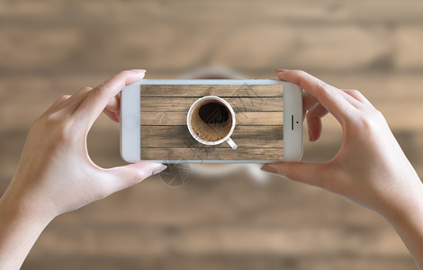 新鲜的相机浓咖啡用手在木制桌子上拍摄白咖啡杯中的热黑用手机照相图片