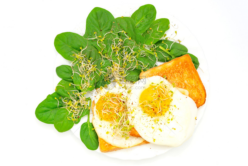 小吃烤面包上煎鸡蛋的顶端景色有菠菜和白盘子上的幼芽豆早晨图片