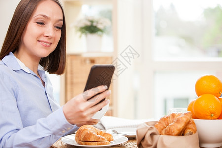 衬衫深褐色微笑的女商人正在家里检查她的电子邮件同时在吃早餐无线的现代图片