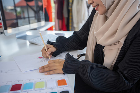 时髦的妇女时装设计师的小企业在服装店工作并使用智能电话和与一起使用的平板电脑精品店织物背景